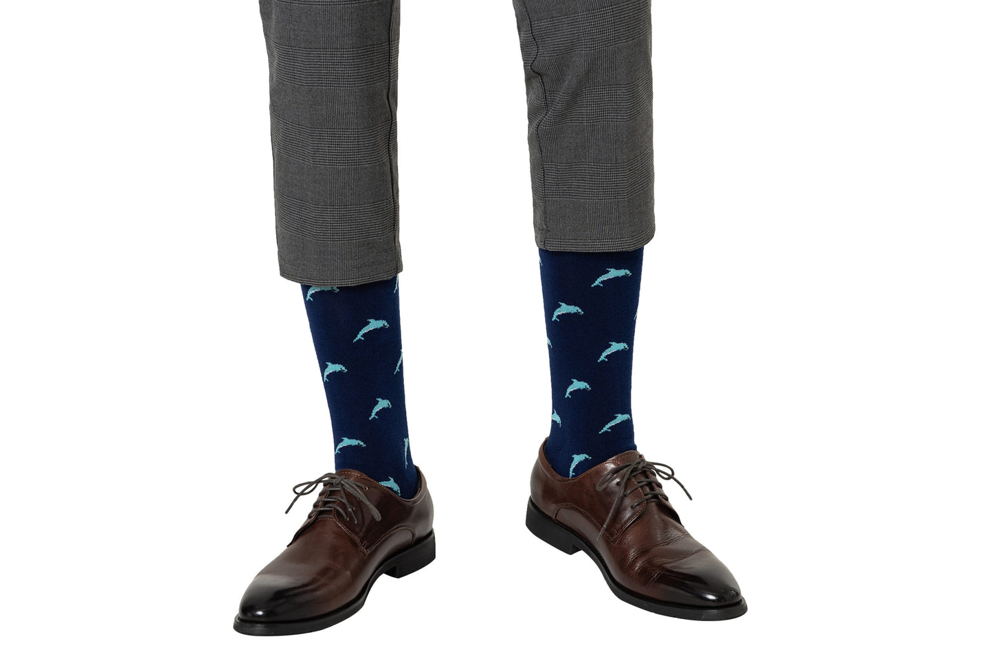 A person shown from the knees down wears gray plaid pants, brown dress shoes, and Dolphin Socks featuring a playful ocean-themed dolphin pattern, all set against a white background.