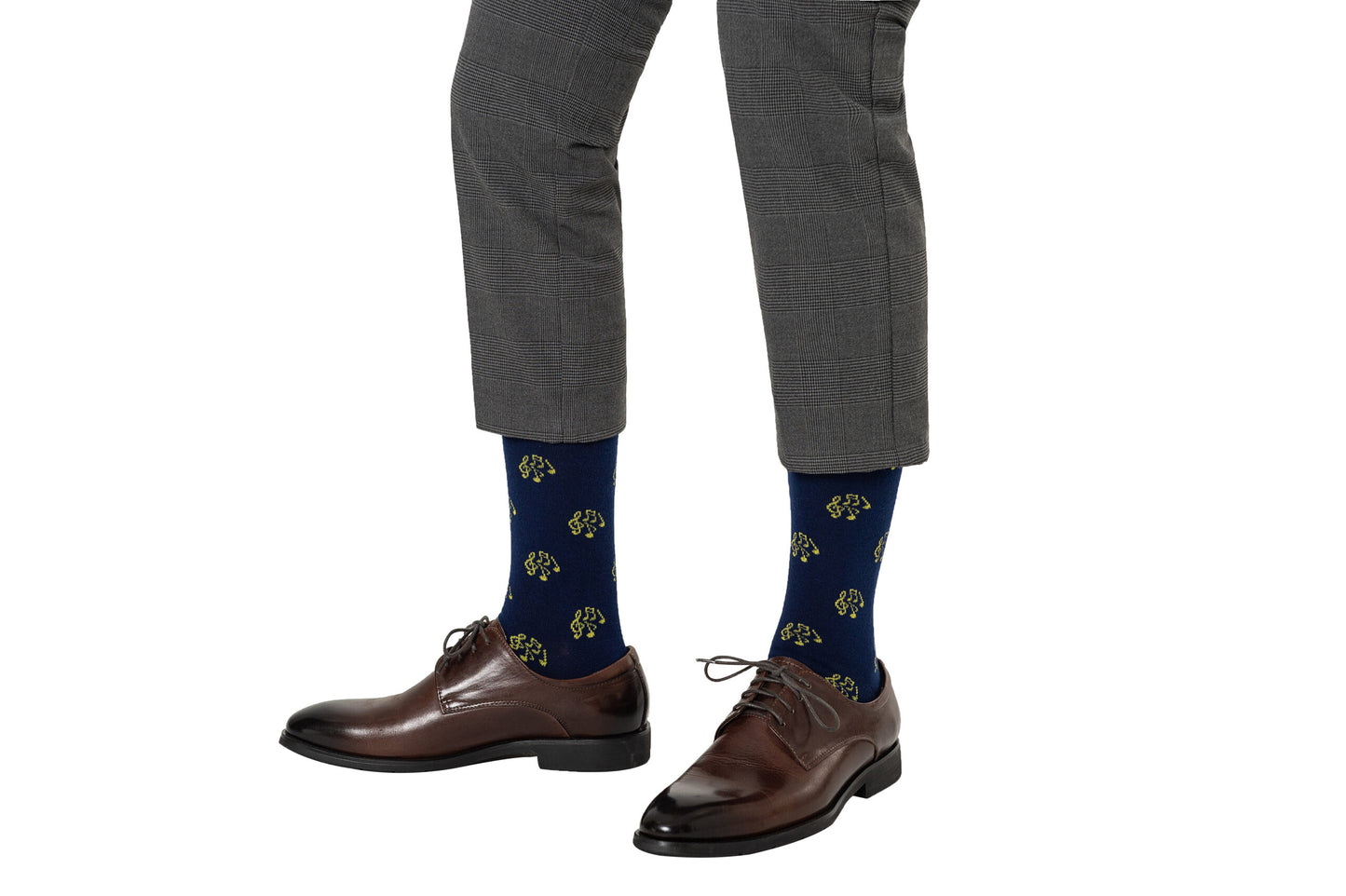 A person wears gray plaid pants, brown dress shoes, and Musical Note Socks—navy blue with a yellow pattern—on a white background. These Musical Note Socks are perfect for musicians and music lovers.