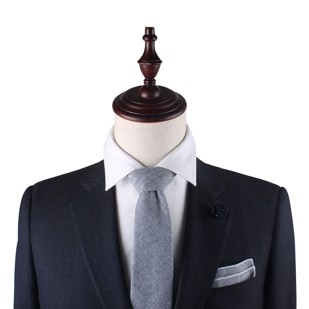 A mannequin dressed in a navy pinstripe suit with a light gray tie, white dress shirt, and adorned with a Navy Blue Herringbone Pocket Square and dark lapel flower exudes elegance.