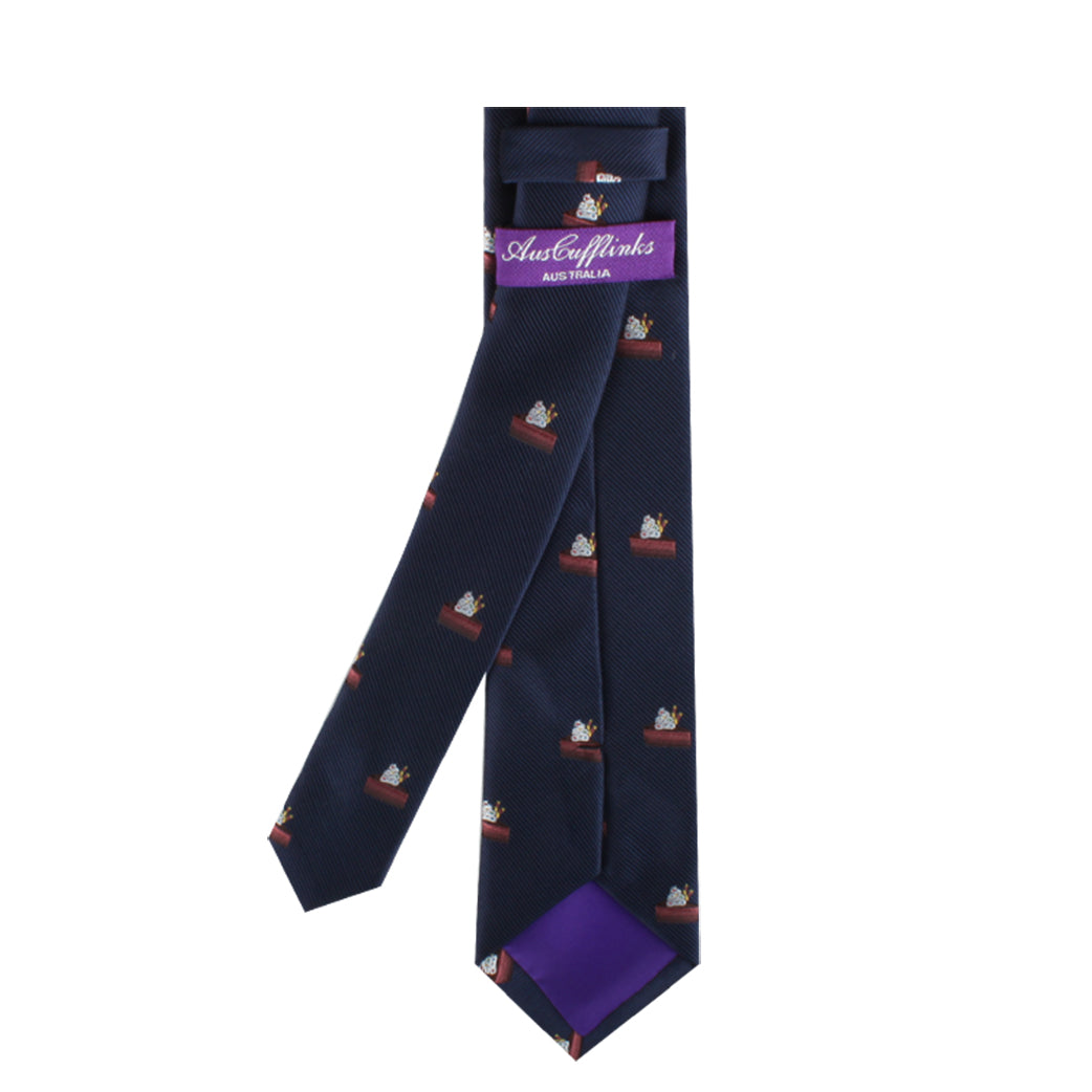 The Cake Skinny Tie, featuring a navy base adorned with a pattern of white surfboards and orange sand, exudes a touch of elegance as it is neatly folded on a white background.