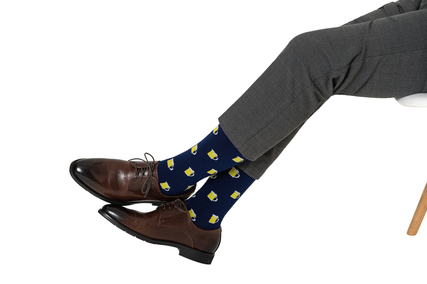 A person in gray dress pants and brown shoes shows off Beer Socks—navy blue socks with a yellow beer mug pattern—perfect for anyone who loves beer.