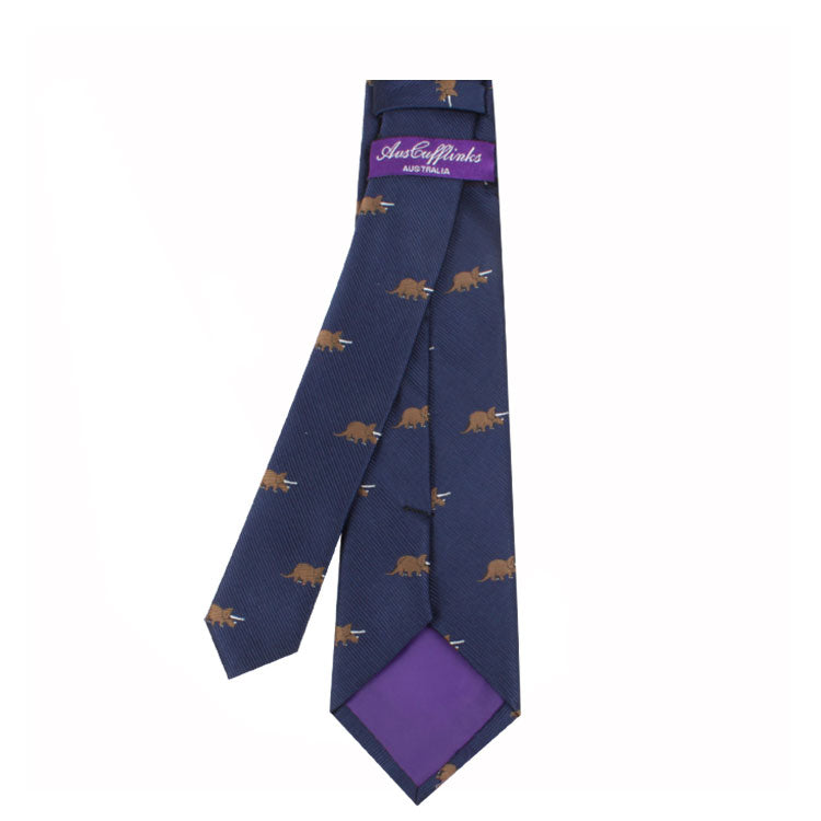 A navy blue Novelty Dino Tie with a pattern of small brown dinosaurs exudes modern elegance and a prehistoric charm. The purple label on the underside features the text "Aubergine Australia.