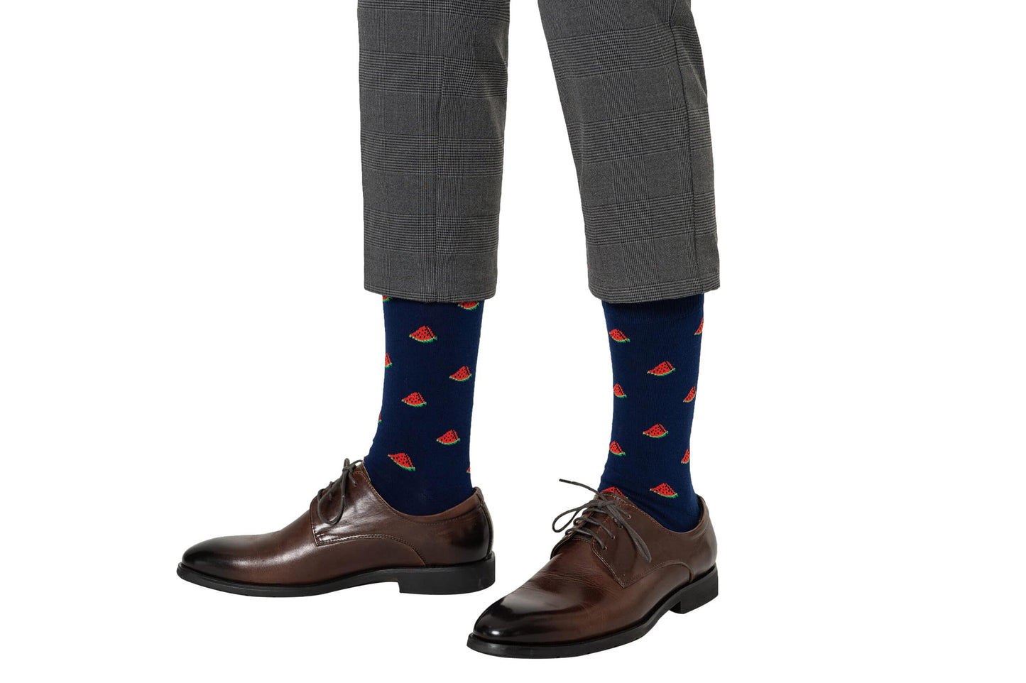 Person wearing Watermelon Socks—navy blue socks with red and green watermelon slice patterns—paired with brown dress shoes and gray plaid pants. A fun gift idea, these breathable socks offer all-day comfort.