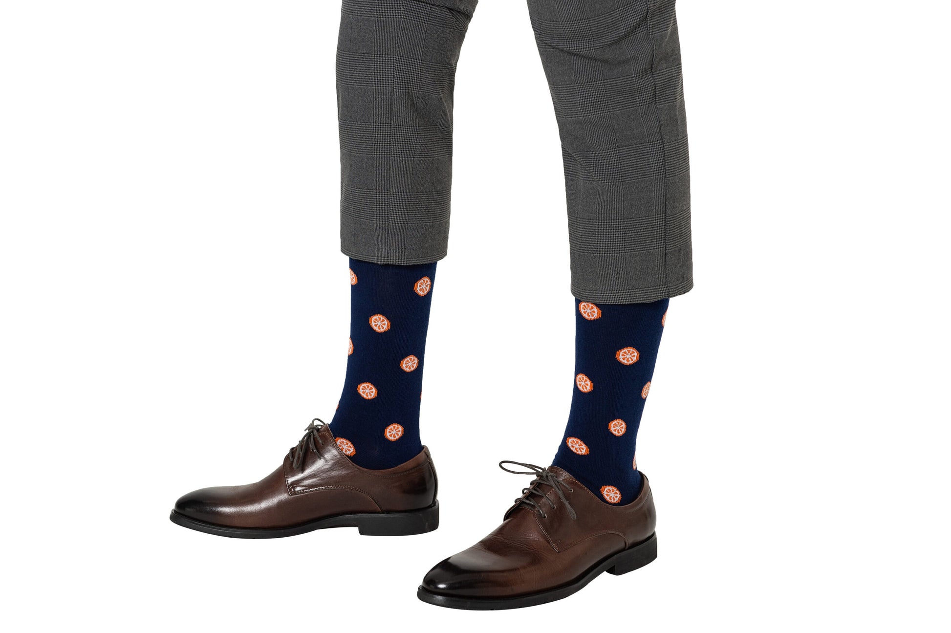 A person showcasing citrusy comfort, wearing brown dress shoes and orange socks with orange coin-pattern details, paired with grey trousers.