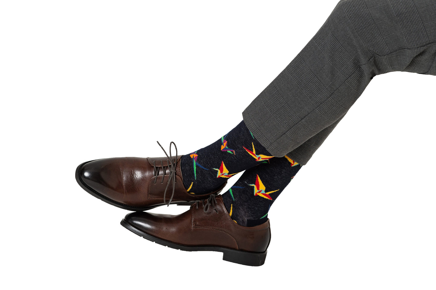 A person wearing brown leather shoes and gray pants highlights dark Origami Socks, featuring colorful origami crane patterns. The ensemble exudes folded finesse, blending perfectly with the crafted comfort of the shoes.
