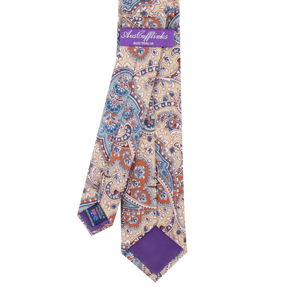 The Blue Latte Brown Paisley Skinny Tie features an elegant paisley pattern in blue, orange, and beige, with a purple underside and a label that reads "AusCufflinks," epitomizing timeless design.