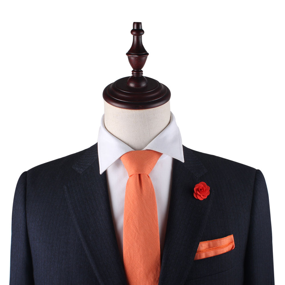The mannequin, featuring a dark suit jacket paired with a white shirt, is complemented by a Peach Orange Skinny Cotton Tie, matching pocket square, and an orange flower pin on the lapel, offering a warm touch reminiscent of spring.