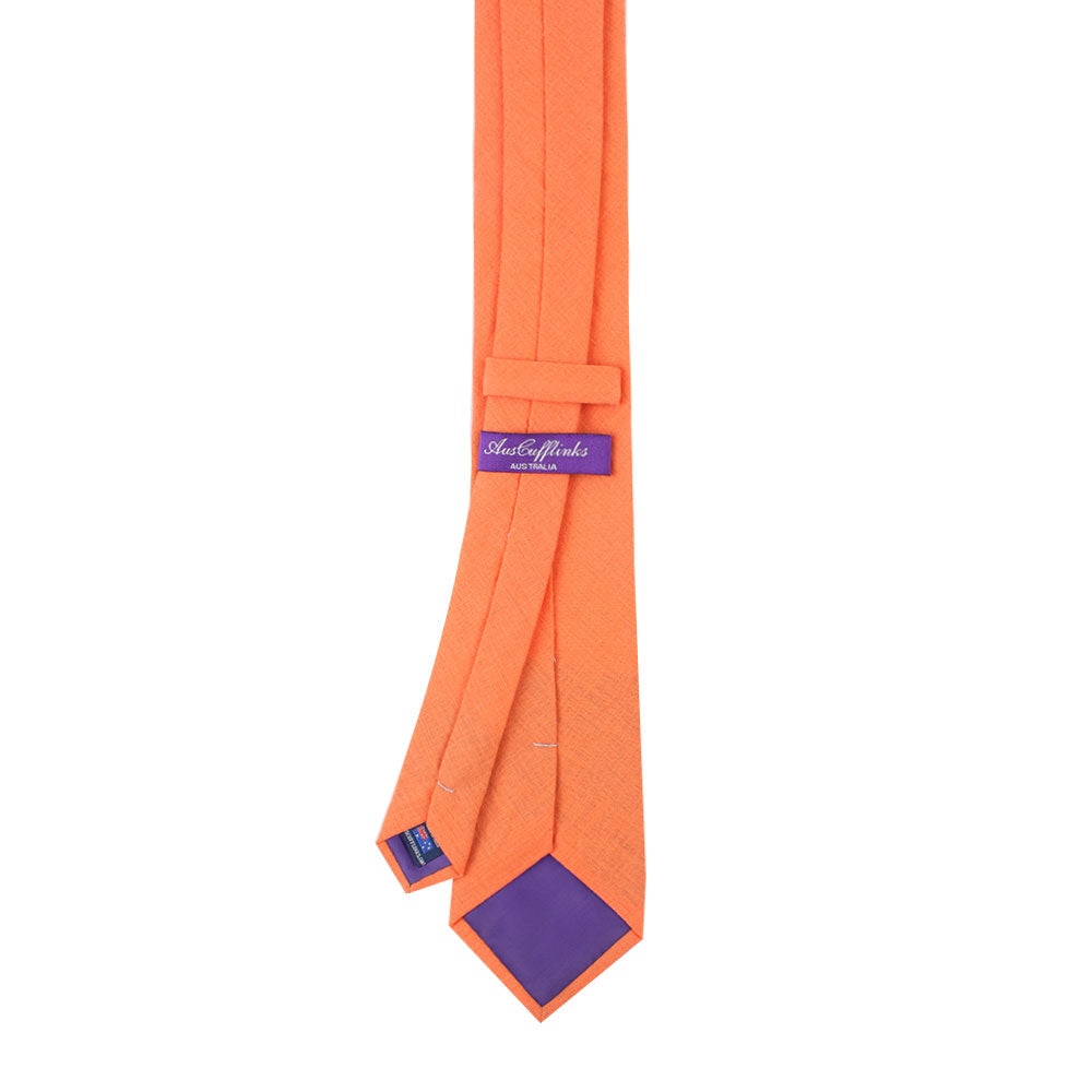 Peach orange skinny tie and pocket square set, showcasing radiant hues, with a blue label and lining. The tie is displayed from the back, highlighting its sleek sophistication with intricate stitching and detailed labeling.