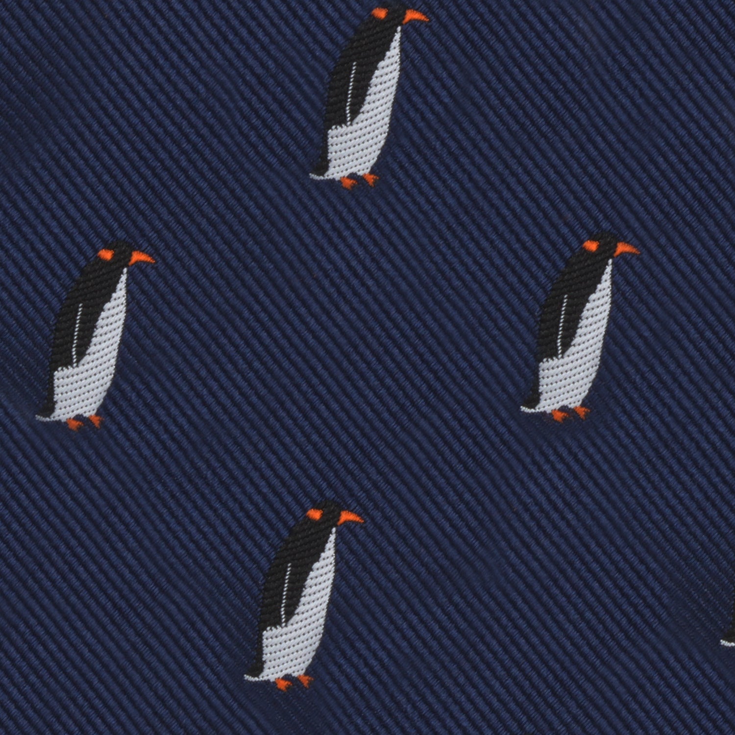 Close-up of a dark blue fabric with an embroidered pattern of penguins with orange beaks and feet, evenly spaced throughout the Penguin Bow Tie, exuding a cold elegance that contrasts beautifully with its charming design.
