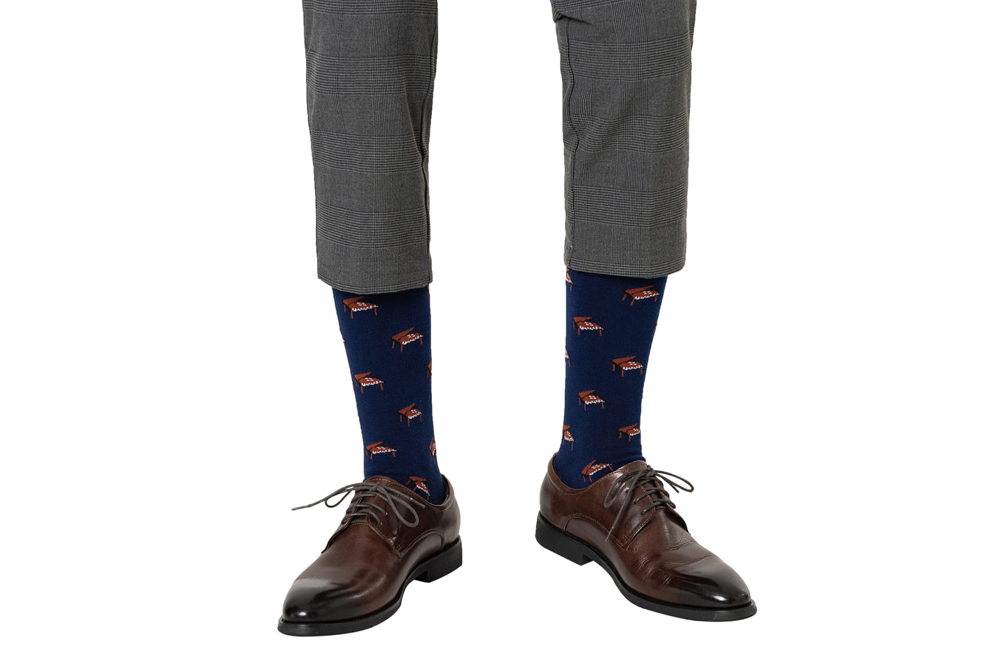 A person wearing gray plaid pants, brown dress shoes, and Piano Socks featuring navy blue color with red and white patterns stands against a white background—perfect as a unique musician gift.