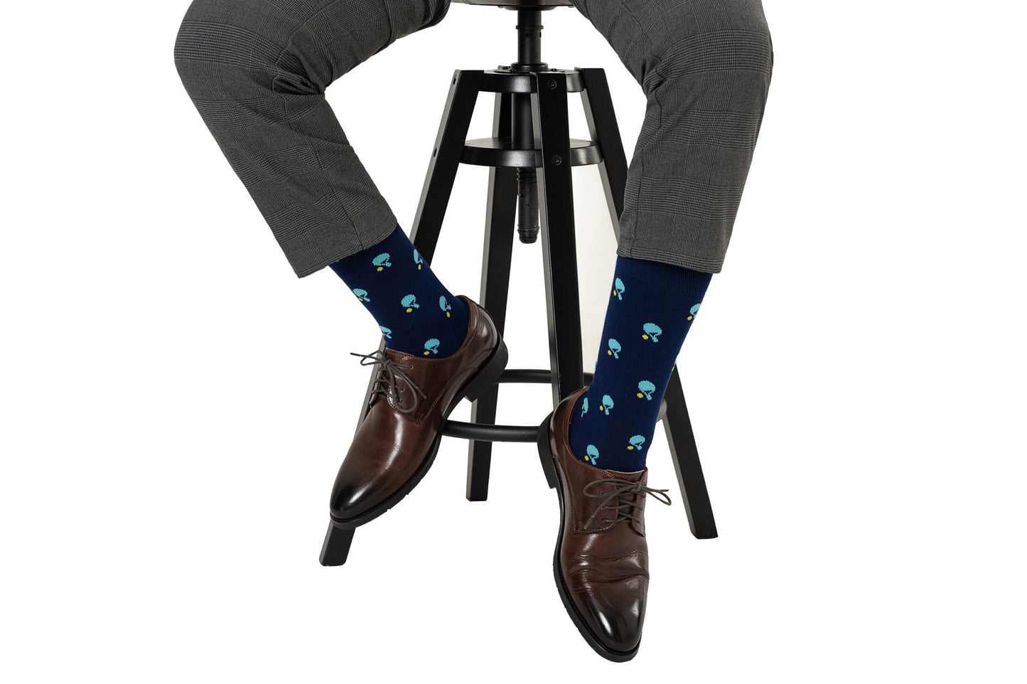 A person in gray plaid pants, brown dress shoes, and Table Tennis Socks sits on a black stool.