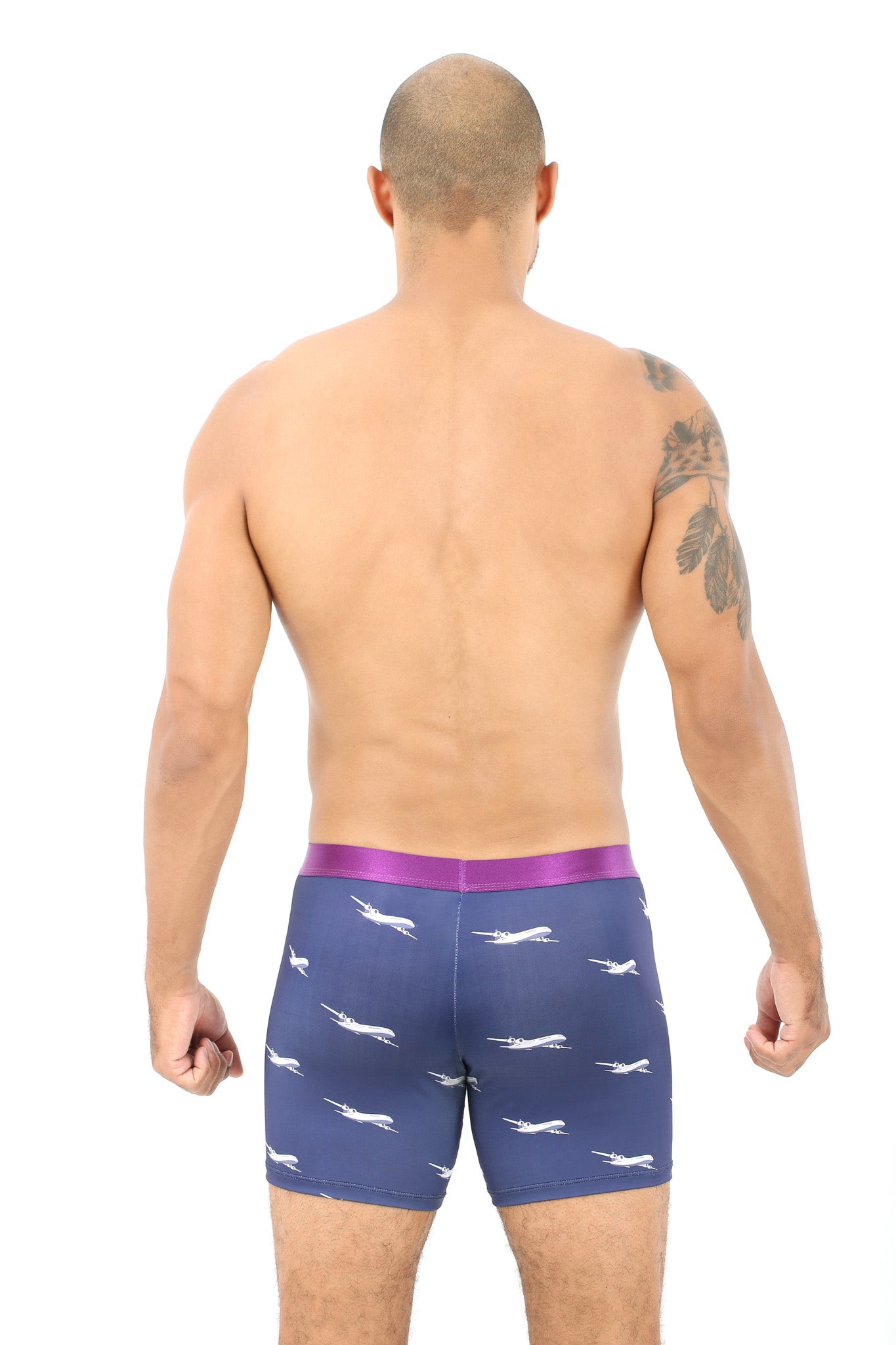 A person stands with their back to the camera, showcasing a cozy style in Airplane Underwear—a pair of blue boxer briefs highlighted by a purple waistband and adorned with a pattern of small airplane prints, ready to take on the skies.