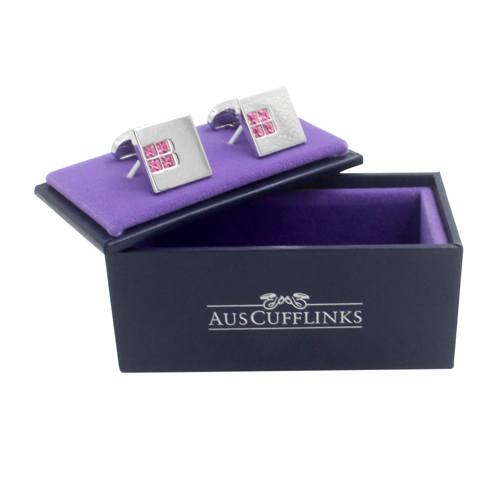 A luxurious pair of Pink Diamonte Cufflinks, featuring pink inlay, is elegantly displayed on a purple velvet holder within an open AusCufflinks box.