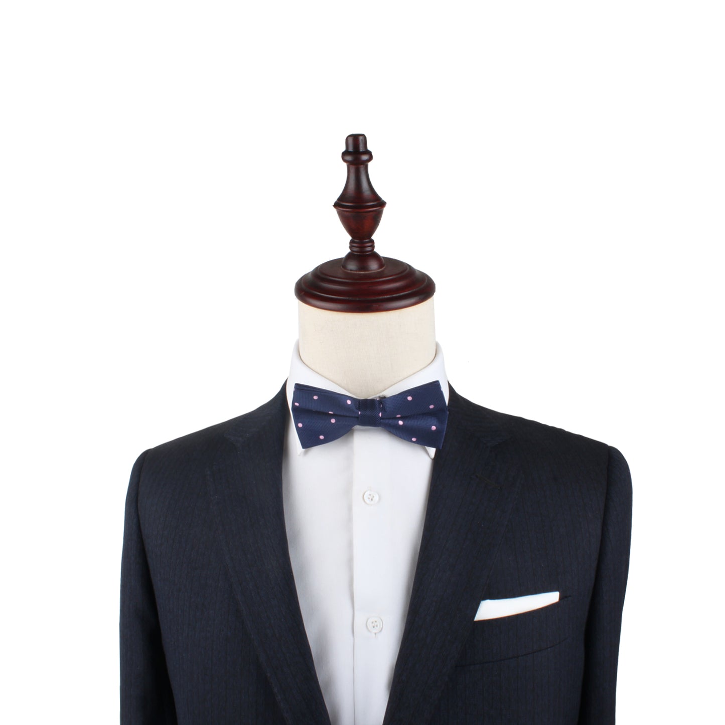 A mannequin dressed in a dark suit with a white shirt and a pink polka dot bow tie, complemented by a white pocket square, exudes soft elegance with its elegant design.