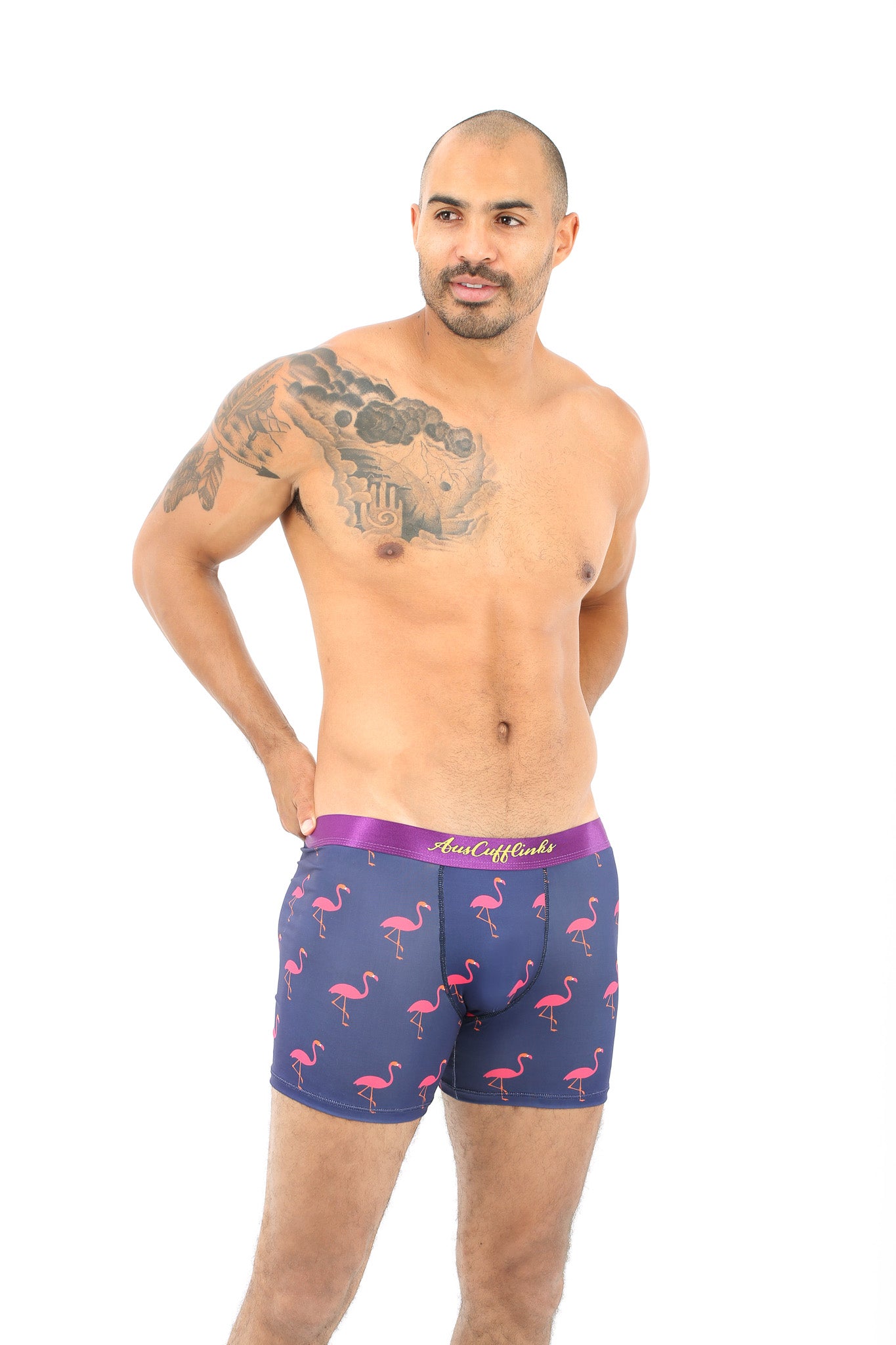 A bald man with a chest tattoo stands confidently in Pink Flamingo Boxer, isolated on a white background.