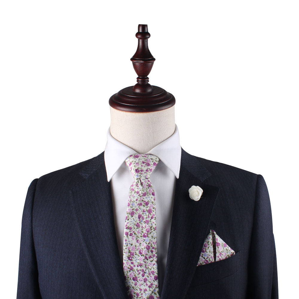 A mannequin in a dark suit with a white shirt is accessorized by the Pink Roses Floral Cotton Skinny Tie and Pocket Square Set, exuding perennial charm against a plain background.