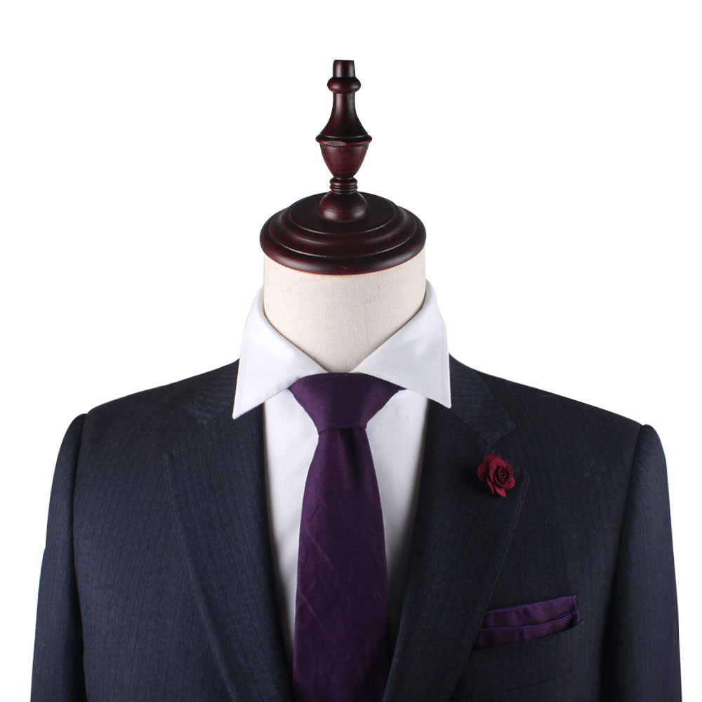 A mannequin in a dark suit and white shirt sports a Purple Cotton Business Tie & Pocket Square Set from AusCufflinks, enhanced by a flower lapel pin against a crisp white background.