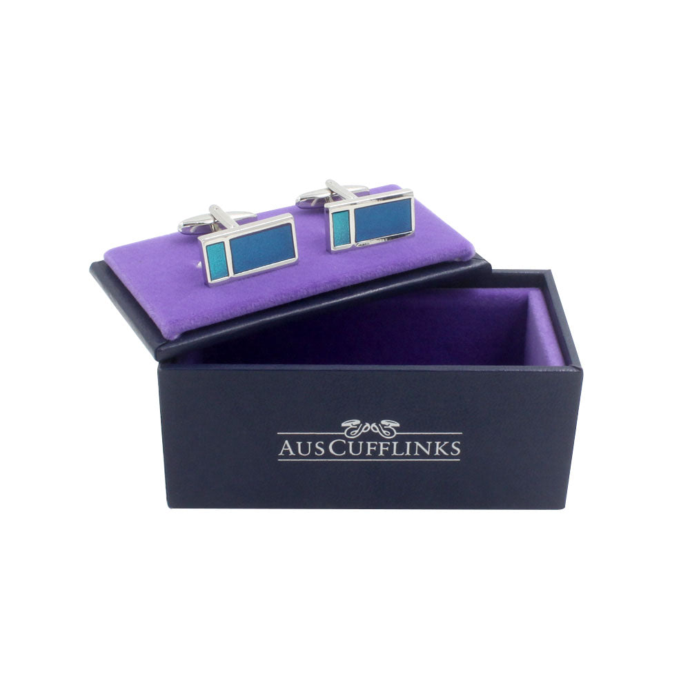 In an open black box with a luxurious purple interior lies a pair of Aqua Rectangle Cufflinks, radiating oceanic elegance.