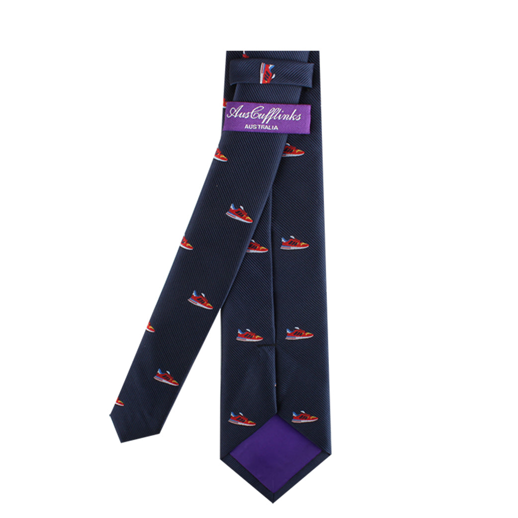A dark blue necktie featuring a red and blue boat pattern, shown front and back. The back of the tie has a purple label displaying the brand "AUSCUFFLINKS," adding urban flair to its modern style, called the Sneaker Skinny Tie.