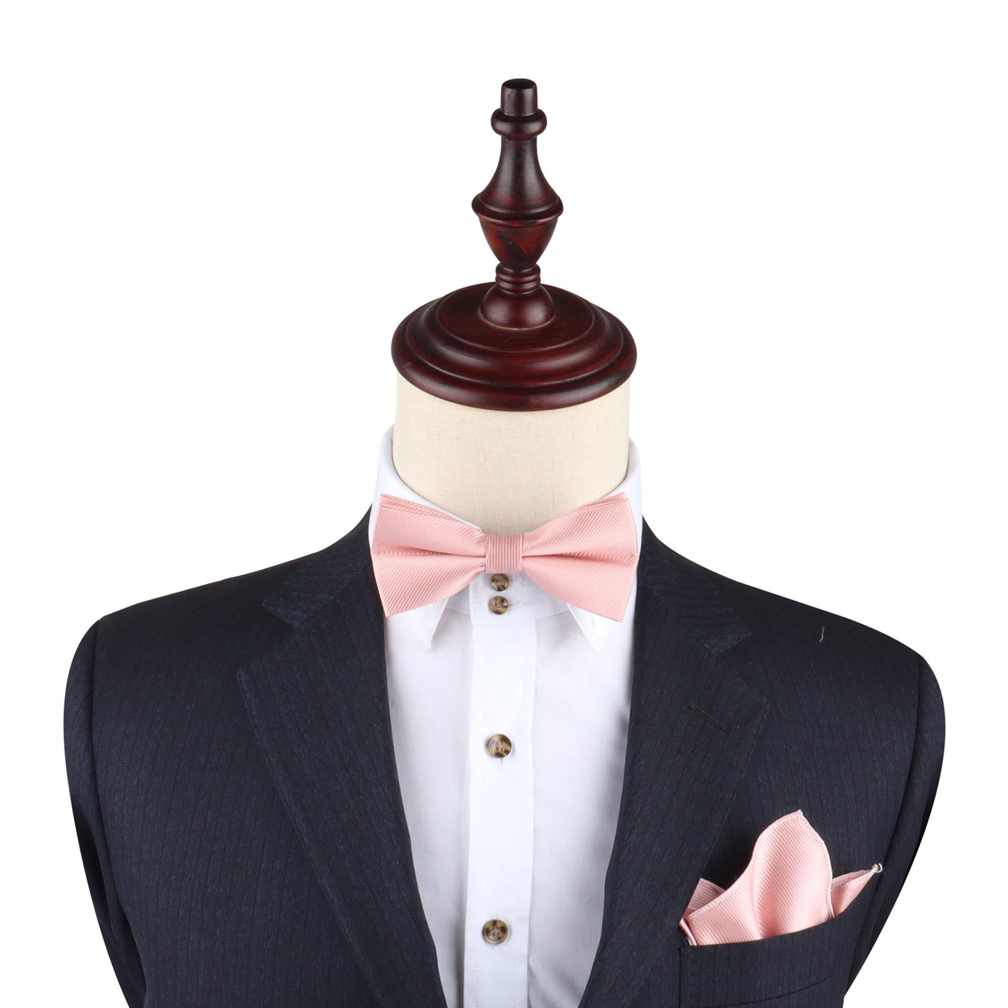 A mannequin presents a formal style with a dark suit, white shirt, and Rose Gold Bow Tie. A matching pink pocket square completes the look. Its wooden stand acts as the head, perfect for black-tie events.