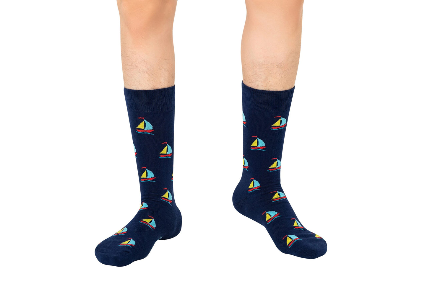 A person stands against a white background wearing Sail Boat Socks—navy blue nautical socks featuring colorful sailboat patterns, perfect for ocean lovers.