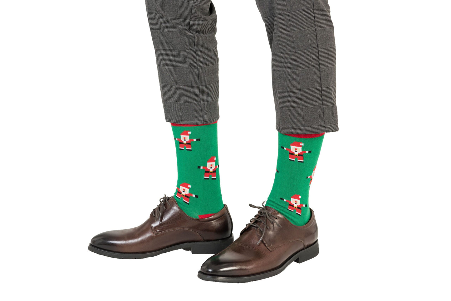 Close-up of a person wearing grey pants, Santa Socks featuring green fabric with Santa Claus patterns, and brown dress shoes, showcasing some festive feet.