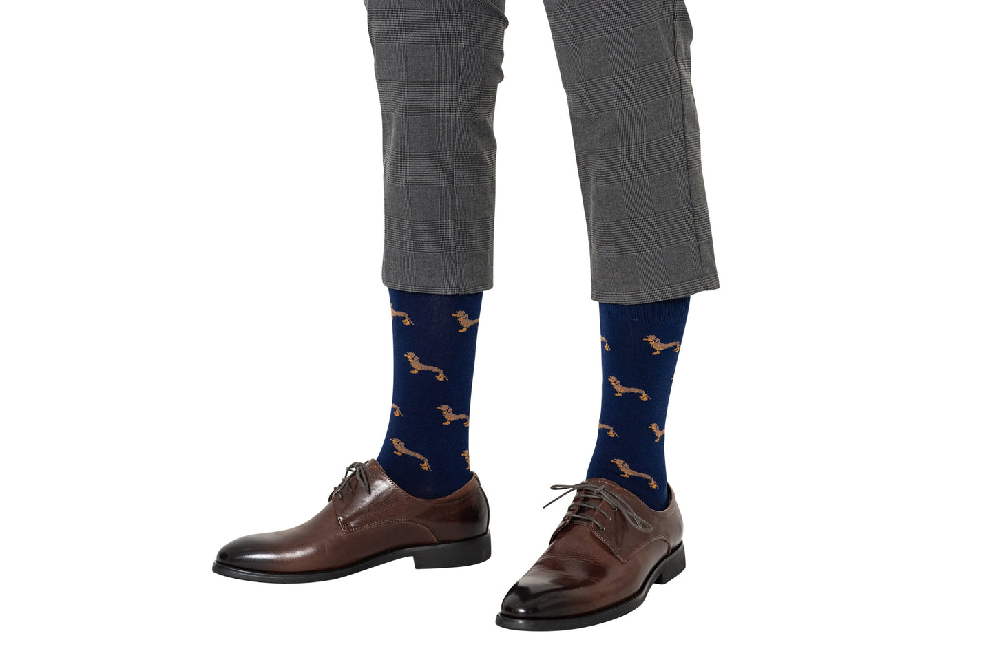 A person wearing gray plaid pants, brown dress shoes, and Sausage Dog Socks featuring navy blue fabric with dachshund patterns.