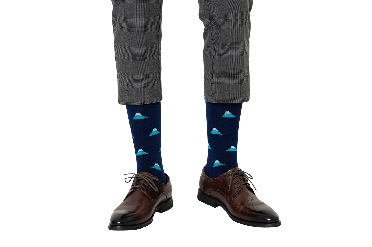 A person showcasing style in gray plaid pants, with Mountain Socks featuring a mountain pattern peeking above brown dress shoes.