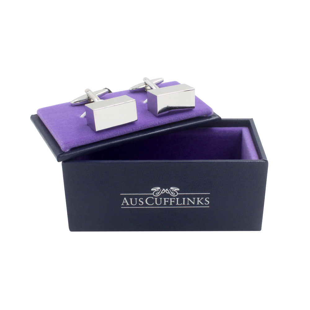 The Rectangle Prism Cufflinks, with a polished silver finish, are elegantly set on a purple cushion in an open black box labeled "AUSCUFFLINKS," exuding timeless sophistication.