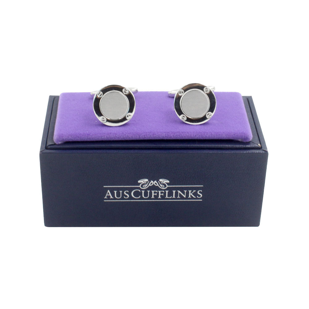 The Inner Circle Silver Cufflinks, with a polished circular design in silver and black, rest charmingly on a purple cushion, nestled in a navy blue AUSCufflinks branded box.