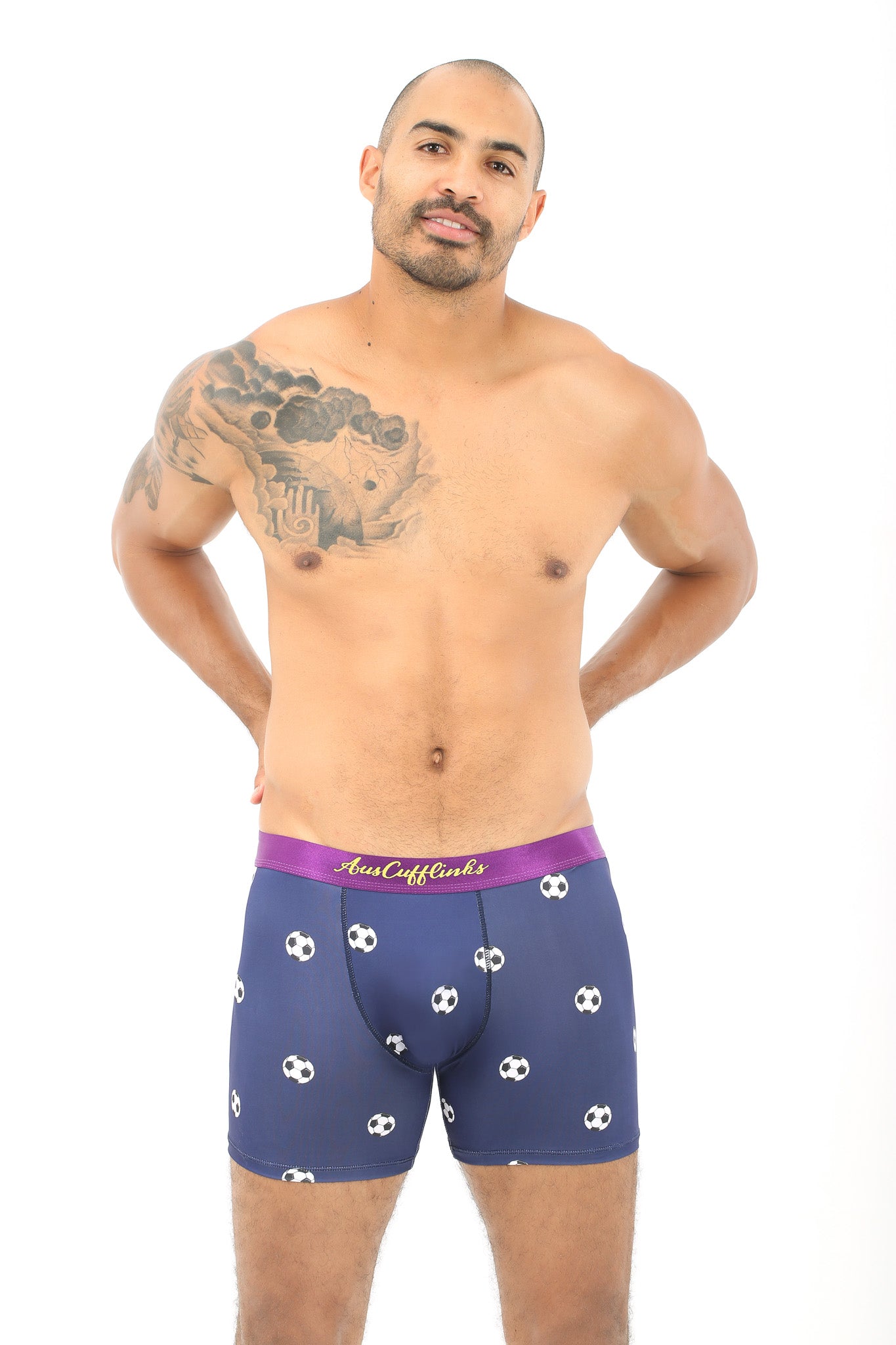 A man embodies comfort while wearing Soccer Underwear, featuring a purple soccer ball print, and showcasing a tattoo on his shoulder against a white background.