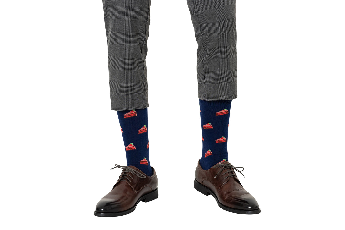 Wearing gray plaid pants, brown dress shoes, and Strawberry Cake Socks—a playful accessory for dessert fans—a person stands against a white background.