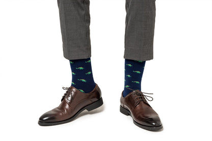 Person wearing brown dress shoes and Stegosaurus Socks with a whimsical alligator pattern, paired with grey trousers exhibiting prehistoric charm.