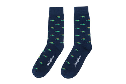 A pair of Stegosaurus socks featuring a whimsical green crocodile pattern and brand logo text on a white background, all adding a touch of prehistoric charm.