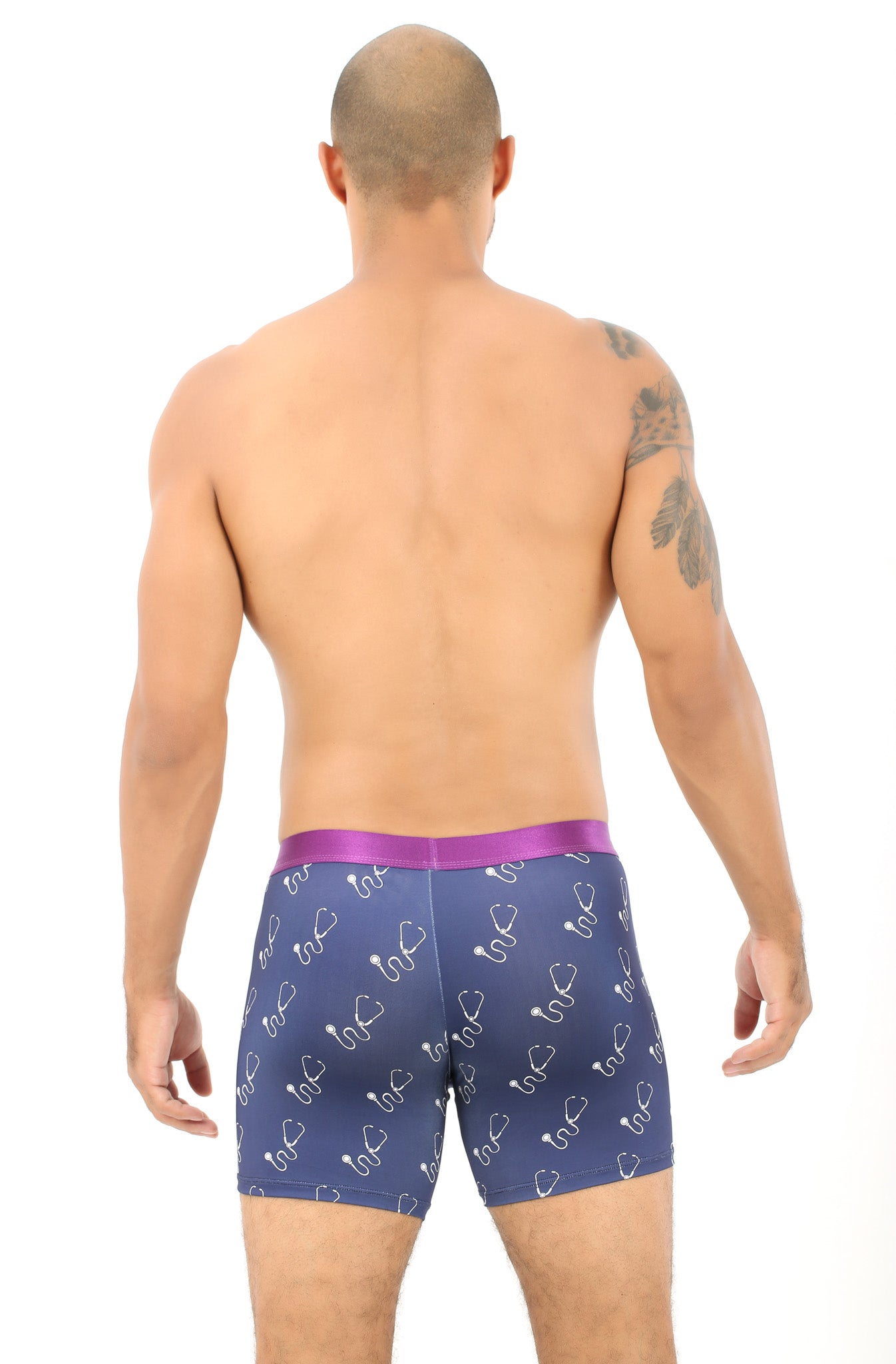 A person with a tattoo on their shoulder stands shirtless, facing away, relishing the comfort of wearing Stethoscope Underwear in purple with a swirl pattern.