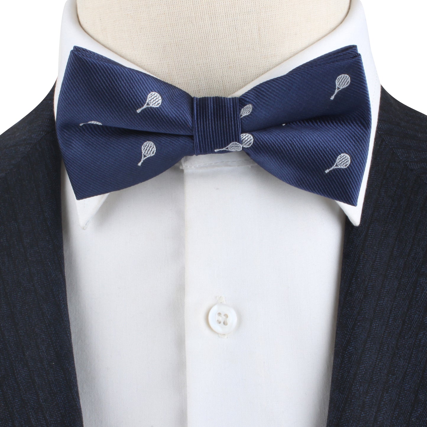 The mannequin sports a dark pinstripe suit with a white shirt and our Tennis Bow Tie, featuring a subtle racket print, perfect for tennis lovers.