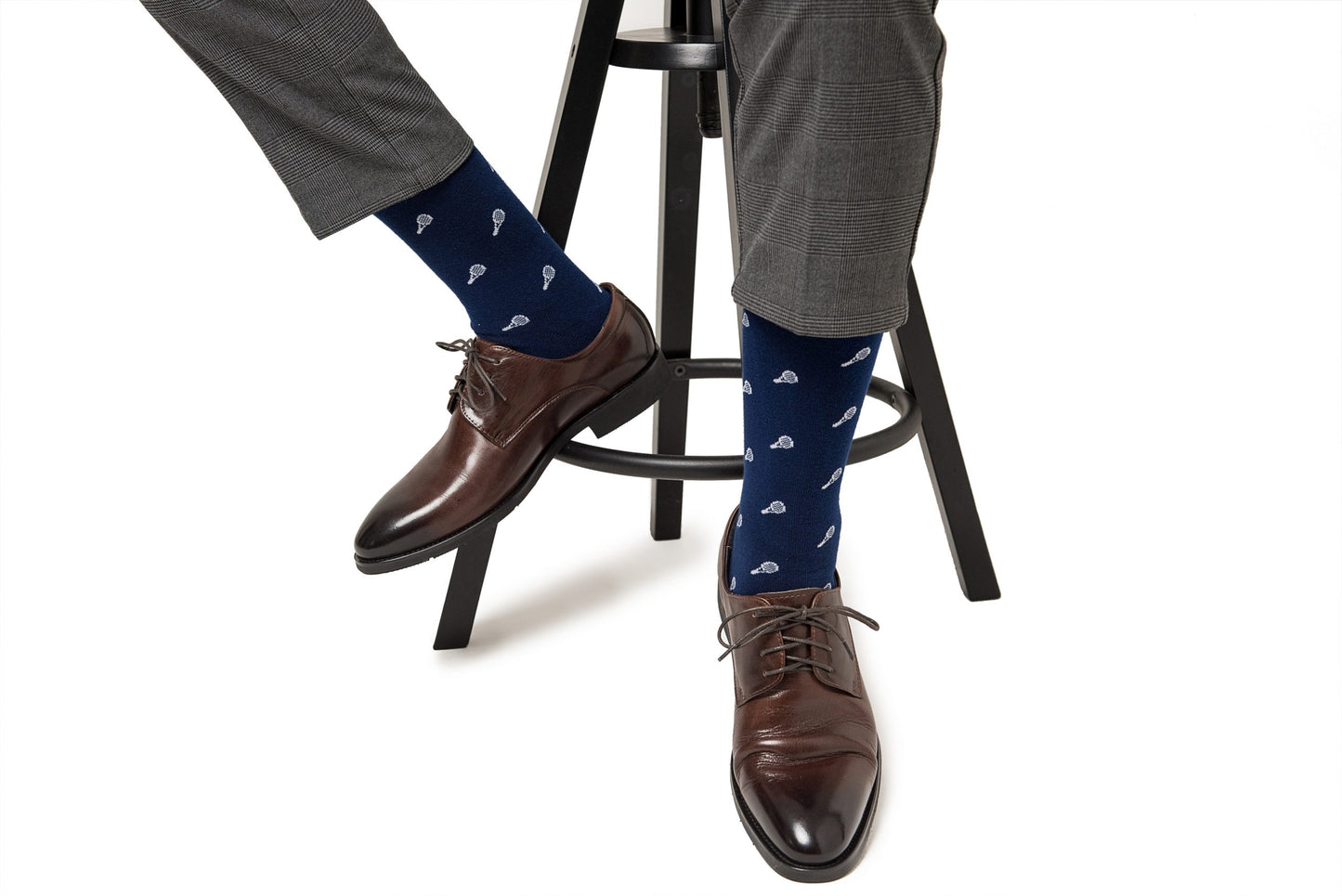 Person wearing gray pants, Tennis Socks, and brown dress shoes, seated on a tall black stool, balancing comfort and style effortlessly for top performance.