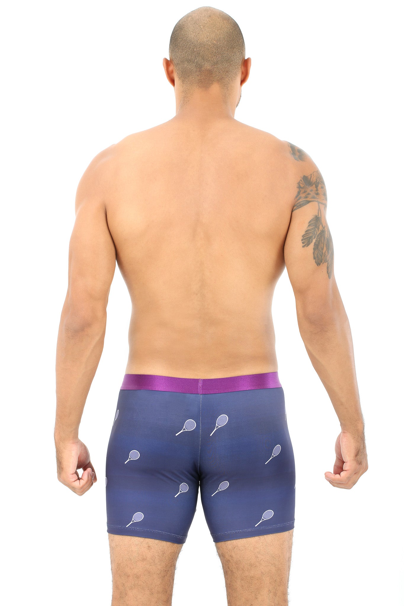 A man with a tattooed arm wears Tennis Underwear, featuring blue boxer briefs with tennis racket designs, viewed from the back. This stylish and comfortable design scores as a winning choice.