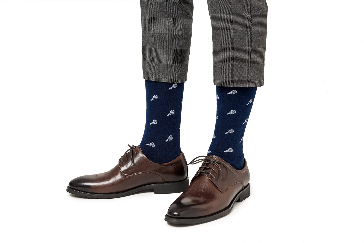 A person wearing gray plaid trousers and brown leather dress shoes with Tennis Socks featuring a pattern of small white paisley designs, striking the perfect balance between comfort and performance.