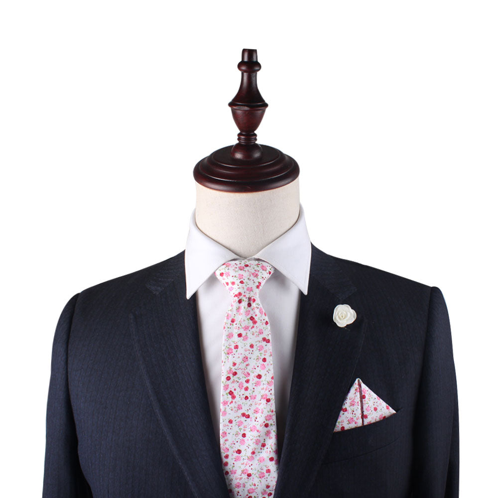 A mannequin dressed in a dark suit with a white shirt, floral tie with subtle light pinks, the Tonal Pink Azalea Floral Pocket Square, and a white boutonniere against a white background. This fashionable man exudes elegance and charm.