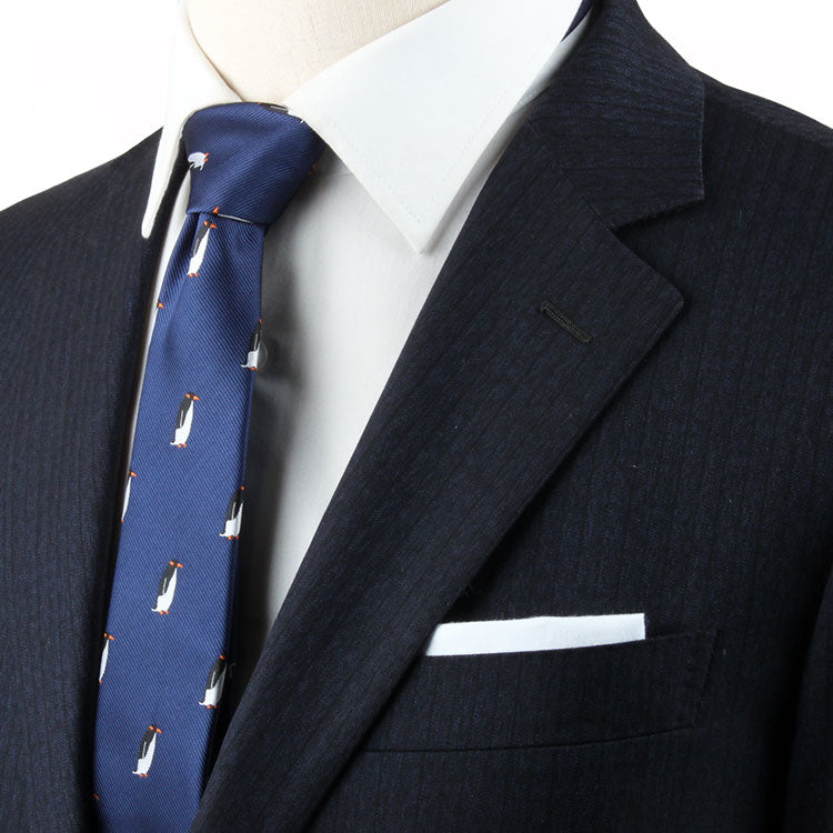 Close-up of a person wearing a pinstripe suit jacket with a white shirt and a Tuxedo Bird Tie featuring small penguin patterns. A white pocket square is tucked into the jacket's breast pocket, adding whimsical charm to the timeless elegance of their attire.