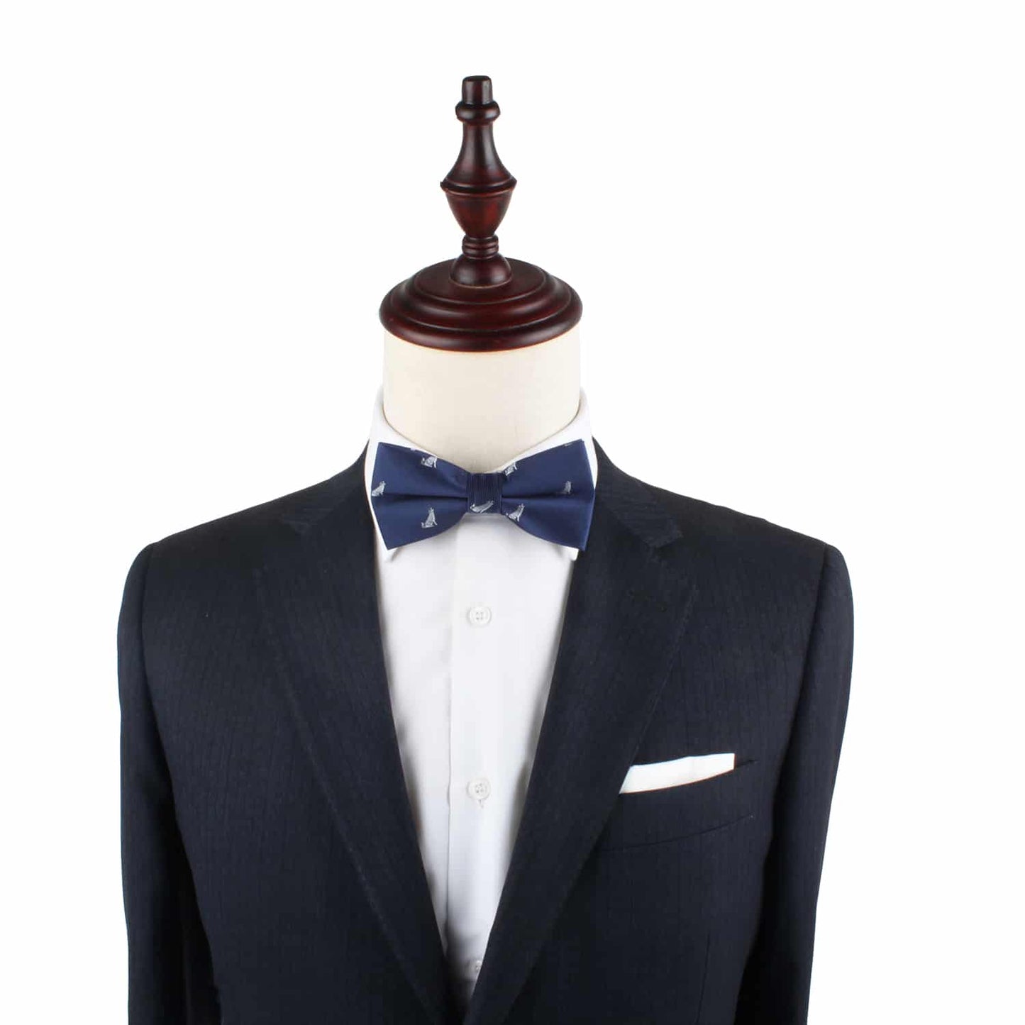 A mannequin displays a tailored dark suit with a white dress shirt, highlighted by the Wolf Bow Tie in navy and a coordinating white pocket square.