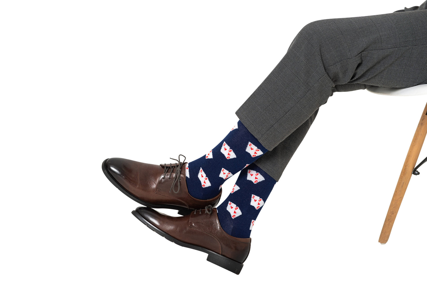 A person in gray dress pants and brown shoes sits with legs crossed, showing off Poker Socks—navy socks decorated with a playing card print, making them the perfect gift for poker players.