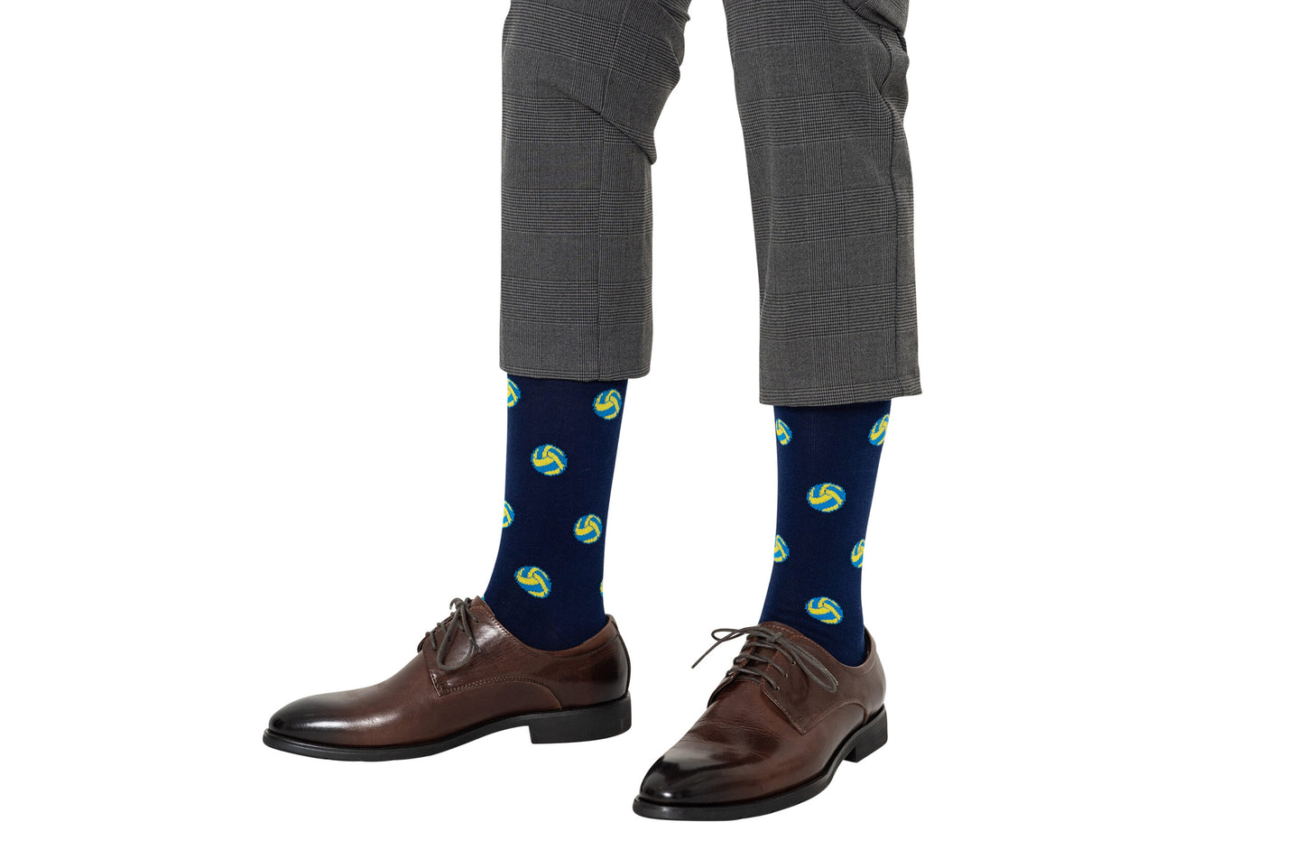 Person wearing gray checkered pants, brown dress shoes, and Volleyball Socks featuring navy blue with green and yellow circular patterns, standing against a white background.