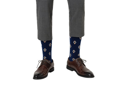 A person wearing grey trousers, dark blue Watch Socks with floral patterns, and polished brown leather shoes, exudes timeless elegance while standing against a white background.
