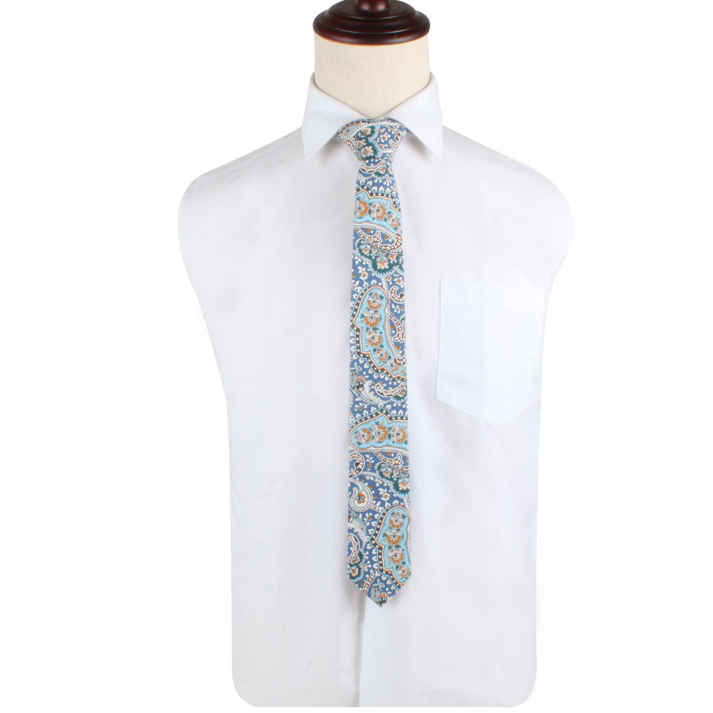 A white dress shirt with a blue paisley skinny tie, featuring an elegant wave-like design, gracefully draped on a mannequin.