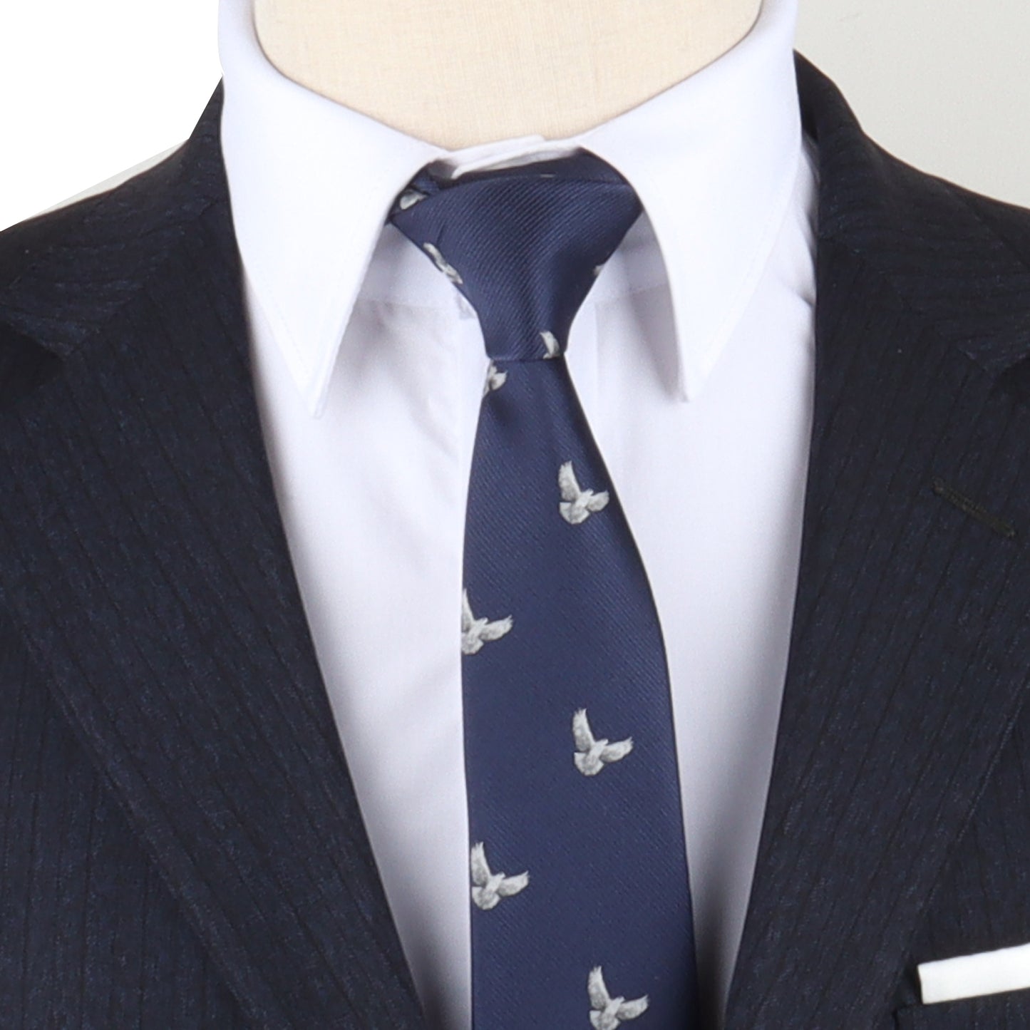 Close-up of a person wearing a dark pinstripe suit with a white dress shirt and a White Dove Skinny Tie featuring a bird pattern, embodying both style and symbolic elegance. Only the chest and neck are visible.