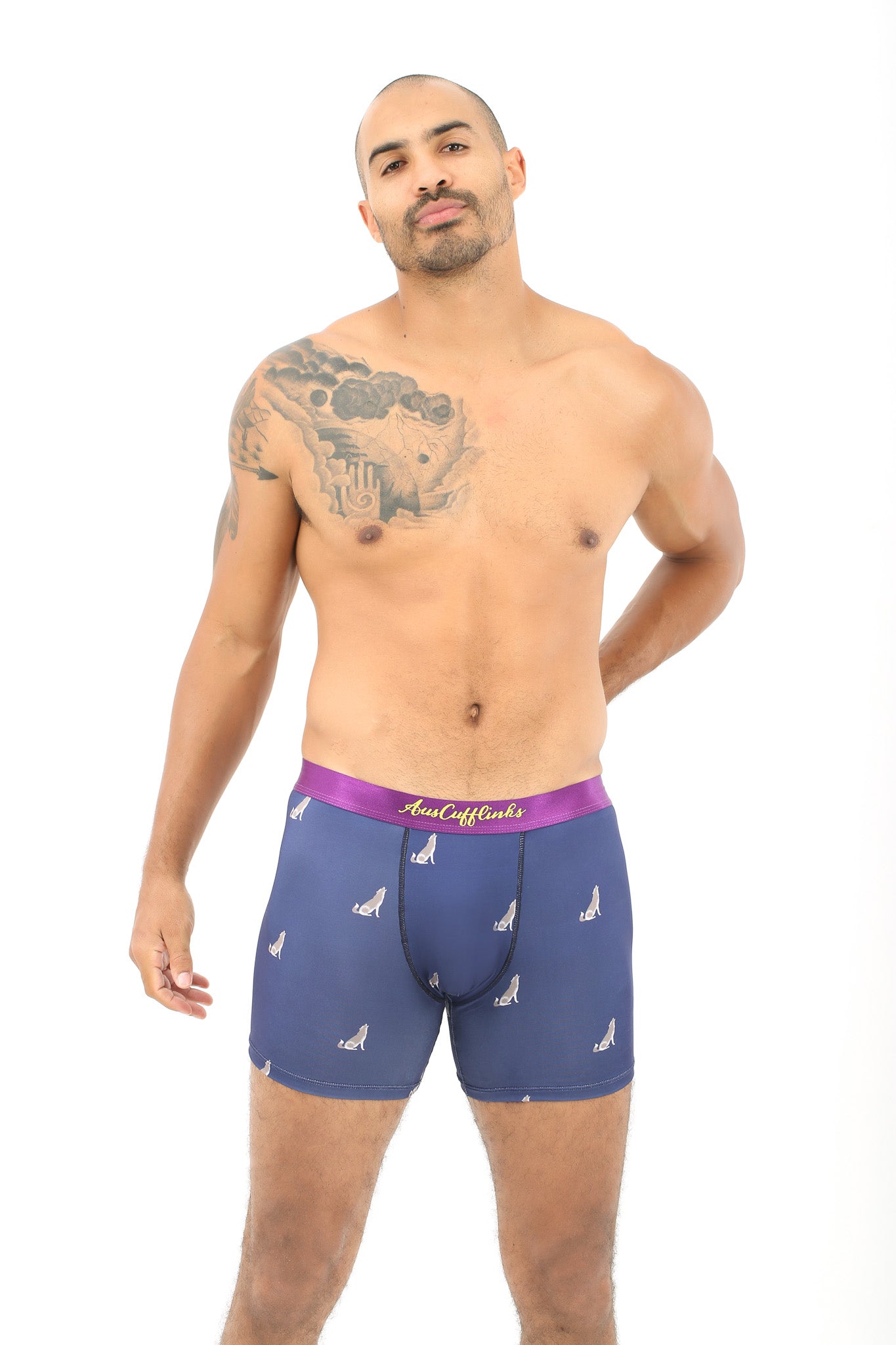 A tattooed man sports Wolf Underwear: blue boxer briefs with a purple waistband and a subtle wolf print, posing against a white background. The design provides a breathable fit for all-day comfort.