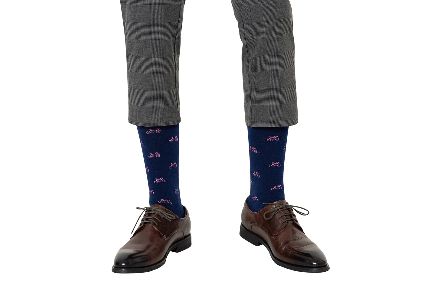 A person wearing grey plaid pants, Pink Bike Socks for a touch of whimsy, and brown leather shoes steps confidently, embracing both style and comfort with every pedal.