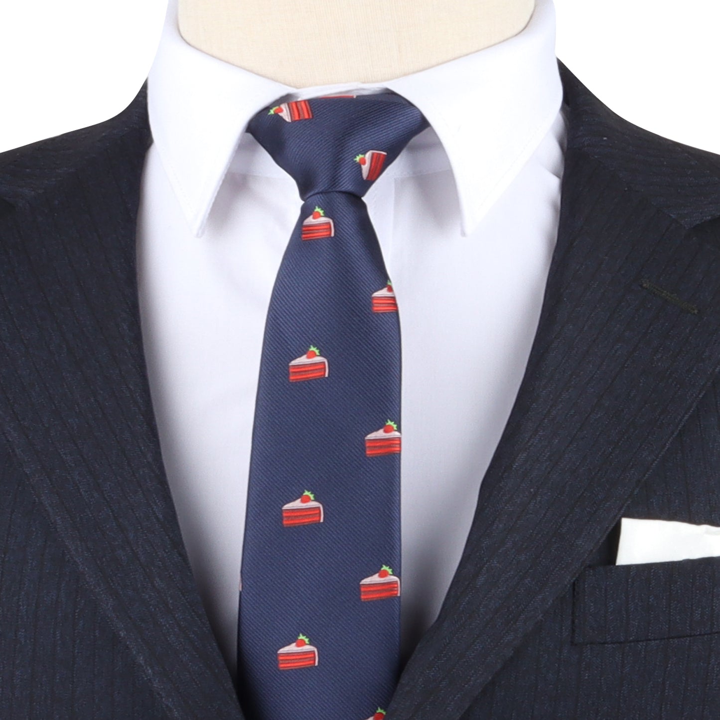 A person wearing a dark pinstripe suit, white dress shirt, and a Strawberry Cake Skinny Tie in navy blue with a red cake slice pattern.